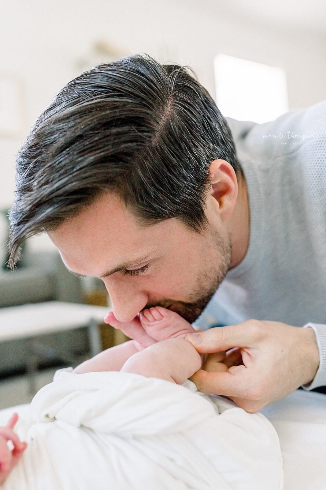 Dad kissing lovingly his newborn baby's tiny toes during in-home lifestyle newborn session in Katy, Texas