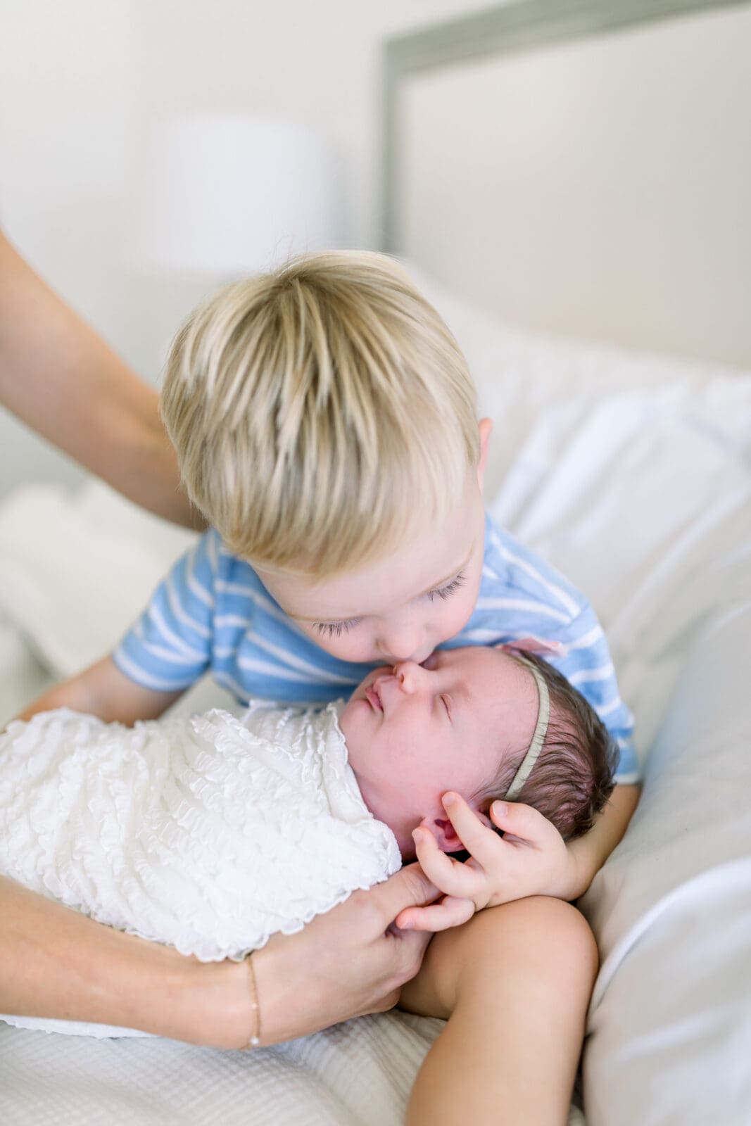 Toddler gently kissing newborn during lifestyle photography session Katy TX