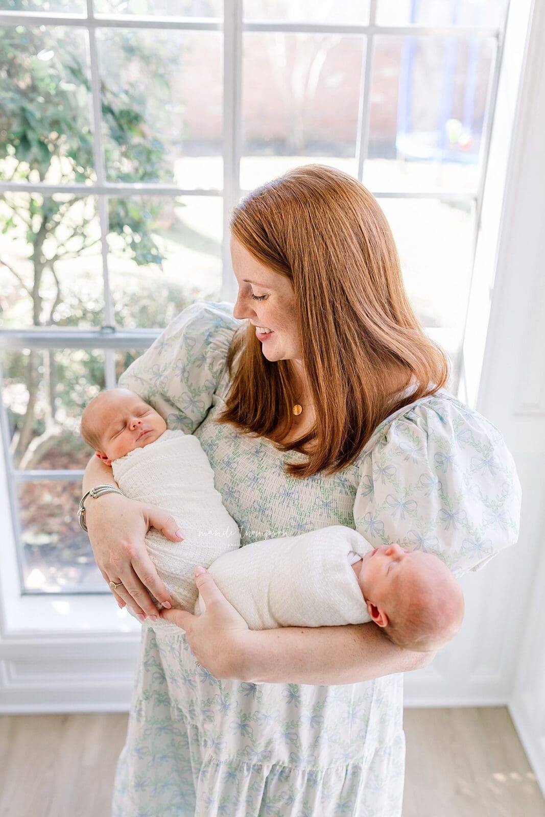 mom in front on large window holding newborn twin babies